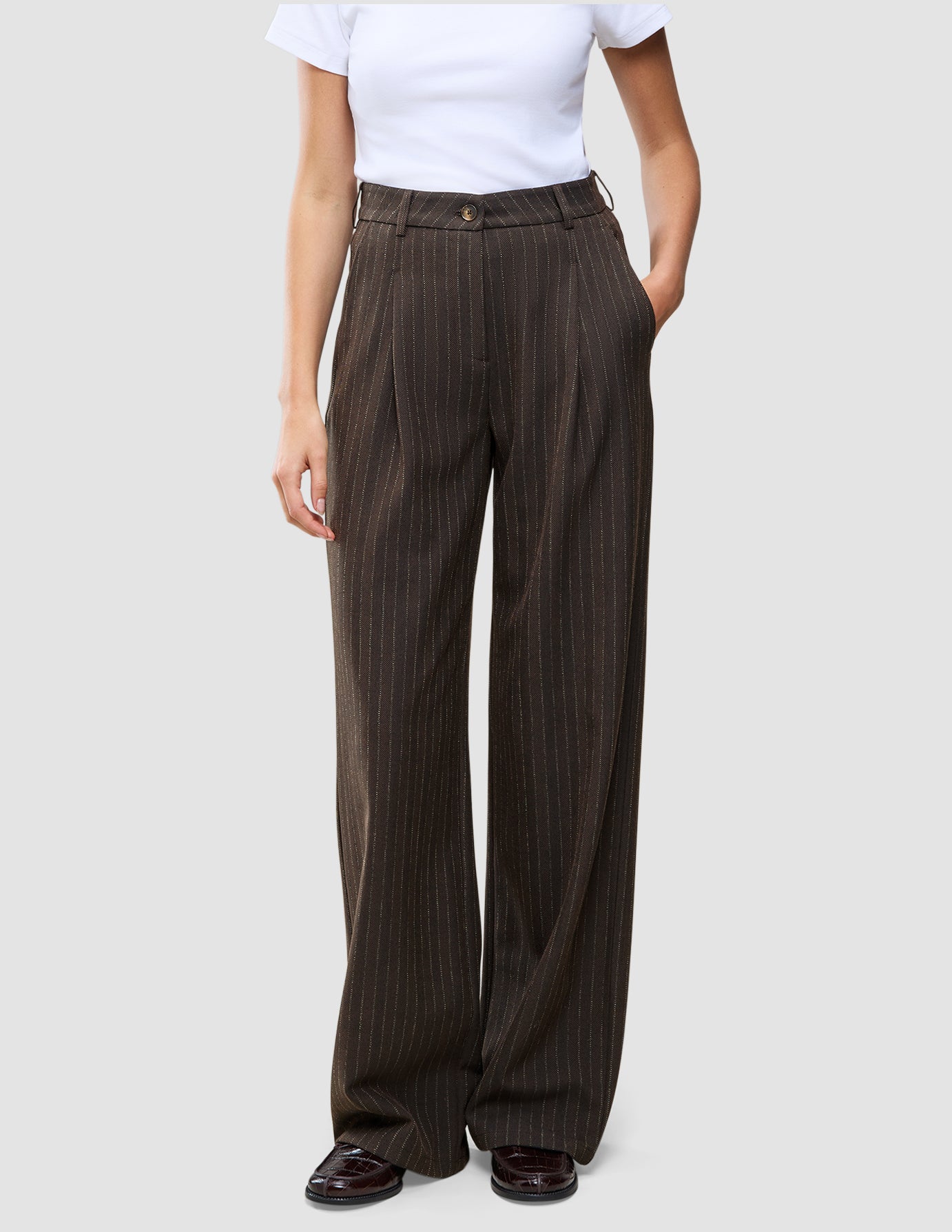 Person iført en hvid T-shirt og Serene Pants Wide Walnut Herringbone – et par højtaljede bukser med brede ben og nålestriber.